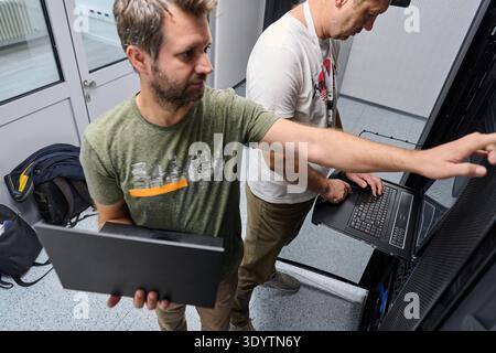 Zwei IT-Techniker beheben bei Servern in einem Rack für Rechenzentren, während sie Laptops verwenden und zusammenarbeiten Stockfoto