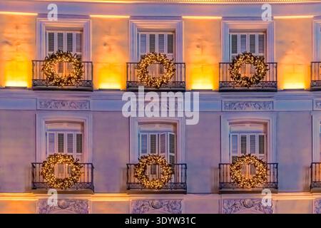 Nahaufnahme von Balkonen, die mit Weihnachtskränzen geschmückt und von warmen Lichtern beleuchtet sind, in Madrid während der Festzeit 2021, Spanien Stockfoto