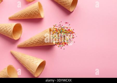 Leere Eiswaffelkegel und bunte Streusel auf rosa Hintergrund, Stockfoto
