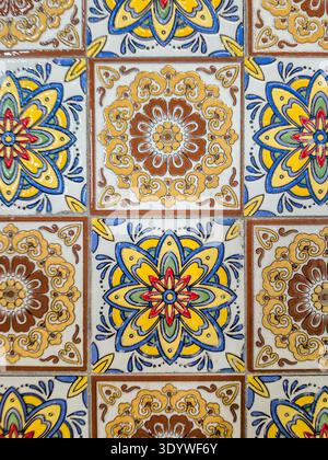 Die Nahaufnahme zeigt ein sich wiederholendes Muster dekorativer Keramikfliesen mit leuchtenden Blumenmotiven und geometrischen Designs Stockfoto