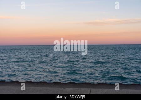 Friedlicher Sonnenuntergang über dem Lake Michigan mit weichem Himmel in Pastelltönen und ruhigem Wasserhorizont. Minimales natürliches Meeresbild mit Kopierraum, fotografiert aus Chicago Stockfoto