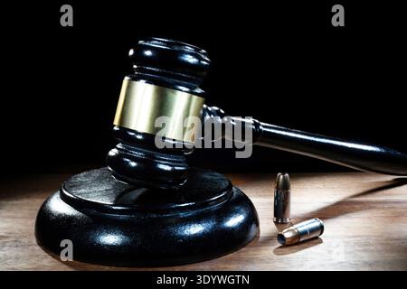 Der Hammer des Richters auf einem Tisch mit dunklem Hintergrund und zwei Pistolenpatronen in der Nähe. Stockfoto