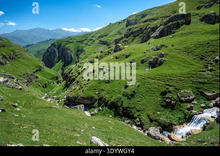 Grüne Berge in Qriz, Aserbaidschan, mit einem kleinen Fluss, der an einem sonnigen Tag durch ein tiefes Tal fließt Stockfoto