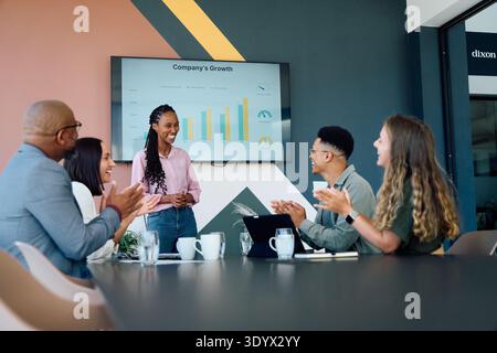 Junge Geschäftsfrau hält Vortrag, während verschiedene Teammitglieder im Büro klatschen Stockfoto