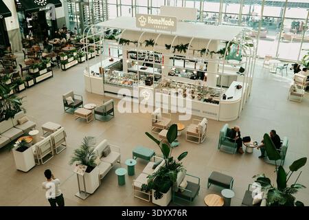 Lebensmittelkiosk und Loungebereich in einem modernen Einkaufszentrum mit Menschen, die sich entspannen und speisen. Belgrad, Serbien – 9. März 2025. Stockfoto