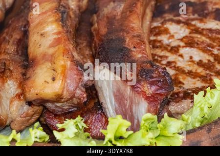 Nahaufnahme gegrillter Schweinerippchen und Steak mit knuspriger bräunlicher Oberfläche, serviert mit frischem Salat als herzhaftes Grillgericht. Stockfoto