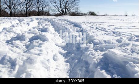 Tiefe Traktorspuren im Schnee nach einem ungewöhnlich starken Schneefall. Fahrzeugspuren im Schnee an einem sonnigen Wintertag. Straßenräumung und Schneeräumung. Stockfoto