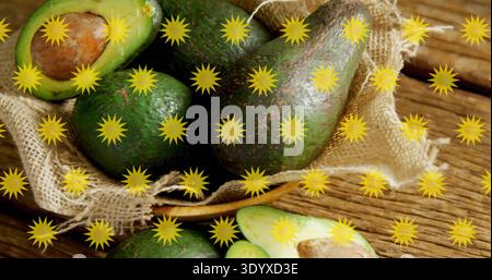 Sie zeigt eine Gruppe reifer Avocados, die auf einem Holztisch in einem Sackleinen-Korb ruhen, gelbe Starbursts Stockfoto