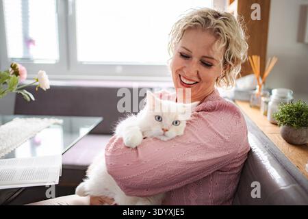 Glückliche Frau, die zu Hause eine weiße Katze kuschelt Stockfoto
