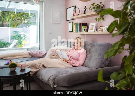 Frau, die sich zu Hause entspannt und gerne auf dem Sofa liest Stockfoto