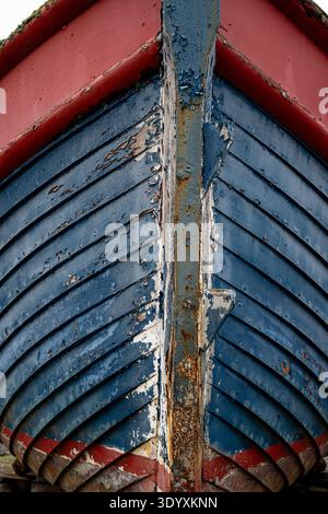Verwitterter Bootsrumpf mit abblätternder blauer und roter Farbe, die maritimen Verfall zeigt Stockfoto