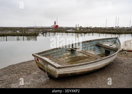 Altes Ruderboot an schlammiger Küste mit Trinity Light Schiff und Holzgebäude in Tollesbury Stockfoto