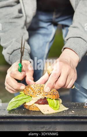 Mann im öffentlichen Stadtpark, der sein Hamburger-Essen zubereitet Stockfoto