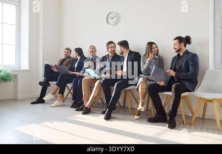 Verschiedene Bewerber chatten und warten auf das Vorstellungsgespräch im Flur des Büros, Lebensläufe Stockfoto