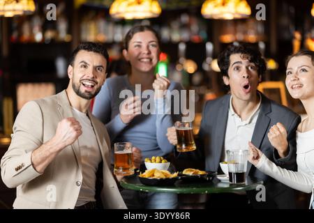 Glückliche Freunde feiern den Sieg ihrer Lieblingsteams, während sie sich das Spiel im Pub ansehen Stockfoto