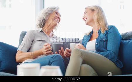 Sprechen Sie, Kaffee und Frau mit einer älteren Mutter auf dem Sofa zu Hause, um Rat, Bindung und Pflege zu erhalten. Lachen, entspannen und weibliche Person mit älterer Mutter im Wohnzimmer Stockfoto