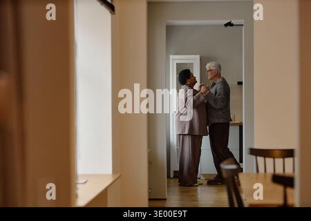 Lächelnder Senior kaukasischer Mann und Senior Black Frau tanzen zusammen drinnen Stockfoto
