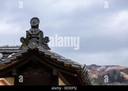 Ein geschnitztes Dämonengesicht onigawara-Dachschmuck auf einem traditionellen japanischen Tempelgebäude mit einem Hügel im Hintergrund in Nara, Japan. Stockfoto