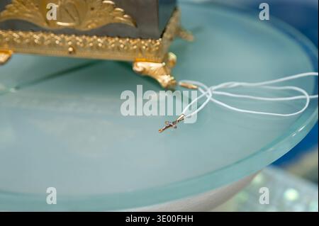 Nahaufnahme eines eleganten goldenen Kruzifix-Anhängers mit Diamanten und weißer Schnur, vorbereitet für Feier oder Zeremonie konzeptionelle Aufnahme eines wertvollen Schmuckgeschenks Stockfoto