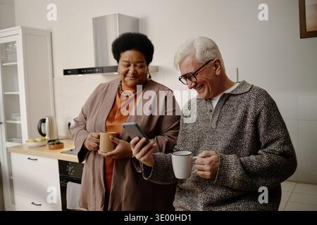 Senior-kaukasischer Mann und Schwarze Frau trinken Kaffee und lachen in der Küche Stockfoto
