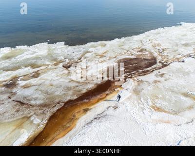 Luftaufnahme eines Mannes, der auf schmelzenden Eisschollen am Rande eines gefrorenen Meeres steht, Frühjahrstaue und Klimaschutzkonzept auf einer Küstenlandschaft Stockfoto