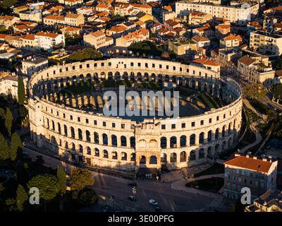 Der Blick aus der Vogelperspektive auf das antike römische Amphitheater steht in krassem Kontrast zur umgebenden modernen Stadt, die im warmen Glanz der untergehenden Sonne, Pul, getaucht ist Stockfoto