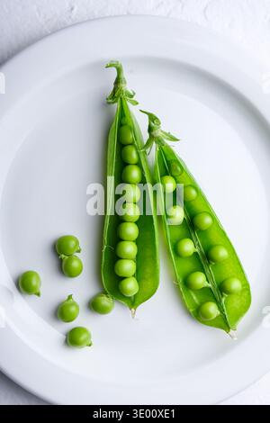 Grüne Erbsen auf einem weißen Teller mit offenen Schoten. Einfaches Styling mit frischen Gemüsezutaten Stockfoto
