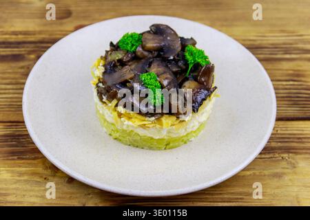 Leckerer mehrschichtiger Salat mit gebratenen Pilzen, Kartoffeln, Eiern, Käse und Mayonnaise auf Holztisch Stockfoto