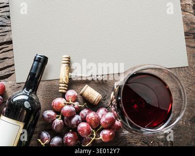 Stillleben von oben mit Rotweinflasche, Glas Rotwein und frischen Trauben auf einem rustikalen Holztisch. Leeres Aquarellpapier bietet Kopierraum für m Stockfoto