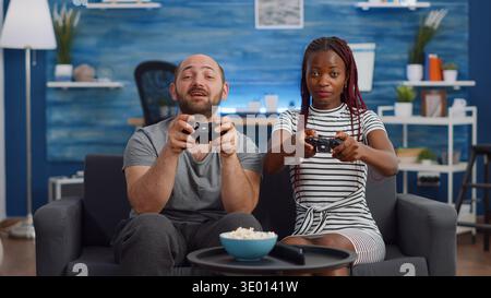 POV von interracial paar mit Controller für Videospiel im Fernsehen im Wohnzimmer. Junge gemischte Rennpartner spielen lustige Aktivitäten auf der Konsole mit Joysticks am Fernseher auf der Couch. Stockfoto