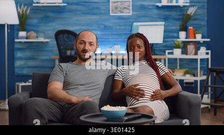Schwanger interracial paar mit Videokonferenz für Remote-Online-Kommunikation zu Hause. Menschen mit gemischter Rasse, die ein Baby erwarten und mit Freunden mit Technologie im Wohnzimmer sprechen Stockfoto