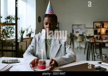 Junge Erwachsene Schwarze Frau Mit Partyhut, Die Allein Sitzt Und Geburtstag Feiert Stockfoto