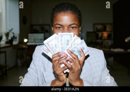 Porträt einer jungen Erwachsenen Schwarzen Frau, die lächelt, während sie Dollarscheine hält Stockfoto