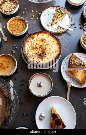 Gebrannte baskische Käsekuchen und Scheiben mit Pistazien, Schokolade und Haselnussbelägen auf dunkler Oberfläche Stockfoto