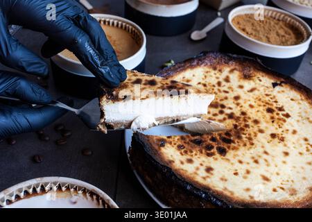 Geben Sie einen schwarzen Handschuh, und servieren Sie eine Scheibe cremigen baskischen Käsekuchen aus einem ganzen Dessert Stockfoto