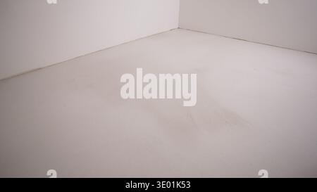 Minimalistischer Blick auf eine leere Zimmerecke. Weiße Wände treffen auf einen hellgrauen, strukturierten Betonboden. Abstrakter architektonischer Hintergrund für CON Stockfoto