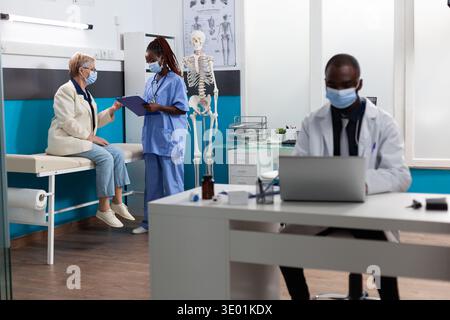 Fachtherapeutin erklärt Krankheitssymptome mit Rentnerin-Patientin, die medikamentöse Behandlung während eines Arzttermins in der Krankenhauspraxis diskutiert. Coronavirus-Konzept Stockfoto
