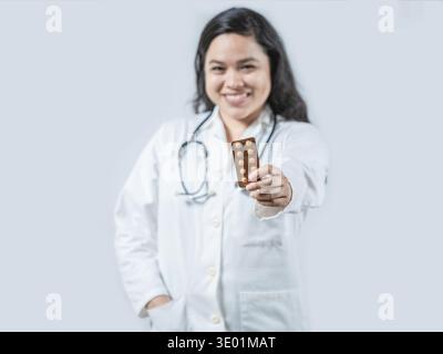 Asiatischer Apotheker zeigt Pillen Tablette isoliert. Lächelnde asiatische Ärztin, die Pillen isoliert hält Stockfoto