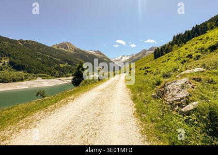 Ein Schotterweg führt in Richtung Speicher Durlaßboden, umgeben von grünen Bergen und Wäldern in Königsleiten Österreich Tirol. Dieses Bild wird aufgenommen Stockfoto