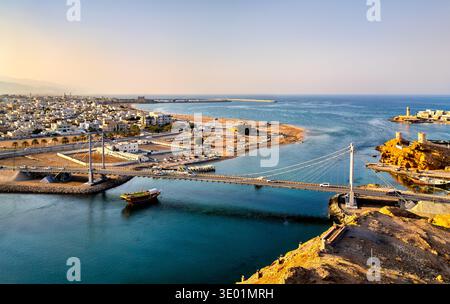 Aus der Vogelperspektive auf die berühmte Al Ayjah Hängebrücke und den historischen Leuchtturm über dem Bach in der Küstenstadt Sur, Oman, Mittlerer Osten Stockfoto