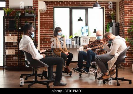 Menschen in Masken bildeten einen Therapiekreis, wobei Psychiater die Diskussion über psychische Gesundheit leiteten. Ältere und junge Individuen, die in einem Mauerraum sitzen und über die Genesung der Alkoholsucht diskutieren. Stockfoto