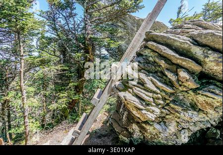 Eine hölzerne Leiter lehnt sich an einen großen Felsen. Der Felsen ist mit Moos bedeckt und hat eine raue Textur. Die Szene ist friedlich und ruhig Stockfoto