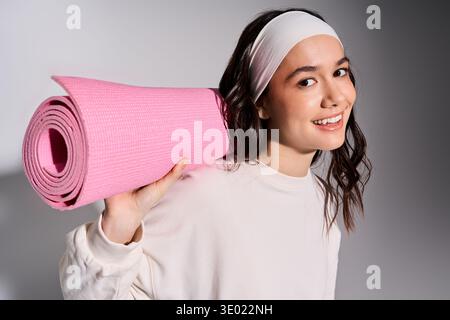 Die energiegeladene Sportlerin mit Kopfbügel genießt im eleganten, grauen Studio die Fitness-Routine. Stockfoto