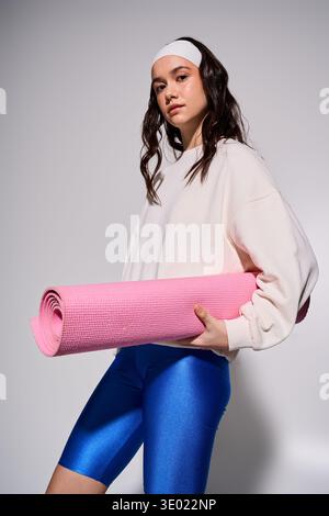 Eine junge athletische Frau mit Stirnband hält eine rosa Yogamatte und bereitet sich auf ein intensives Workout vor. Stockfoto