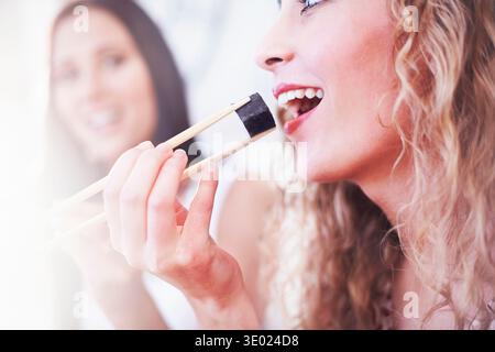 Nahaufnahme von zwei Freundinnen, die Sushi mit Essstäbchen in der Küche essen Stockfoto
