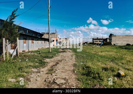 Dirt Road durch das sich entwickelnde Viertel in Mlolongo, Kenia – informelle Siedlung und Bau unter dem blauen Himmel Stockfoto