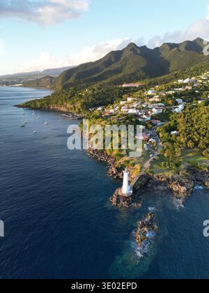 Aus der Vogelperspektive eines weißen Leuchtturms, der Wache an der felsigen Küste steht, wo das tiefblaue Meer auf das grüne Land trifft, Guadeloupe, Guadeloupe. Stockfoto