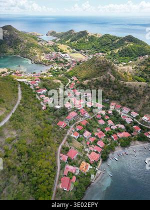 Blick aus der Vogelperspektive auf die Häuser mit rotem Dach, eingebettet in üppig grüne Hügel, treffen auf das ruhige türkisfarbene Wasser der Karibik, Guadeloupe, Guadelo Stockfoto