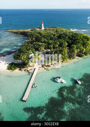 Blick aus der Vogelperspektive auf einen Leuchtturm auf einer grünen Insel, umgeben von türkisfarbenem Wasser, einem Dock, der sich bis ins Meer erstreckt, Guadeloupe, Guadeloupe. Stockfoto