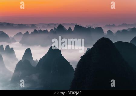 Aus der Vogelperspektive der zerklüfteten Gipfel, die unter einem lebendigen Sonnenaufgang durch ätherischen Nebel durchdringen, Yangshuo, China. Stockfoto